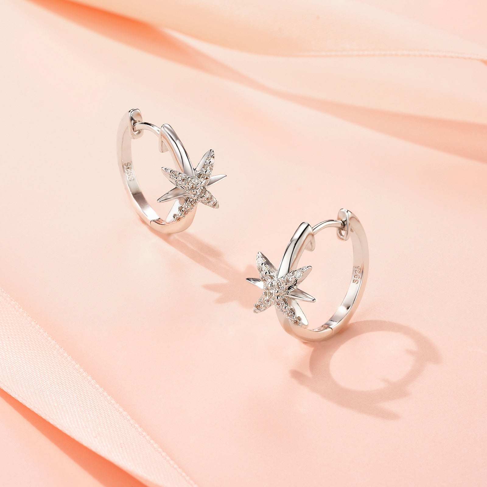 Celestial north starburst moissanite huggie hoop earrings resting on pink fabric.