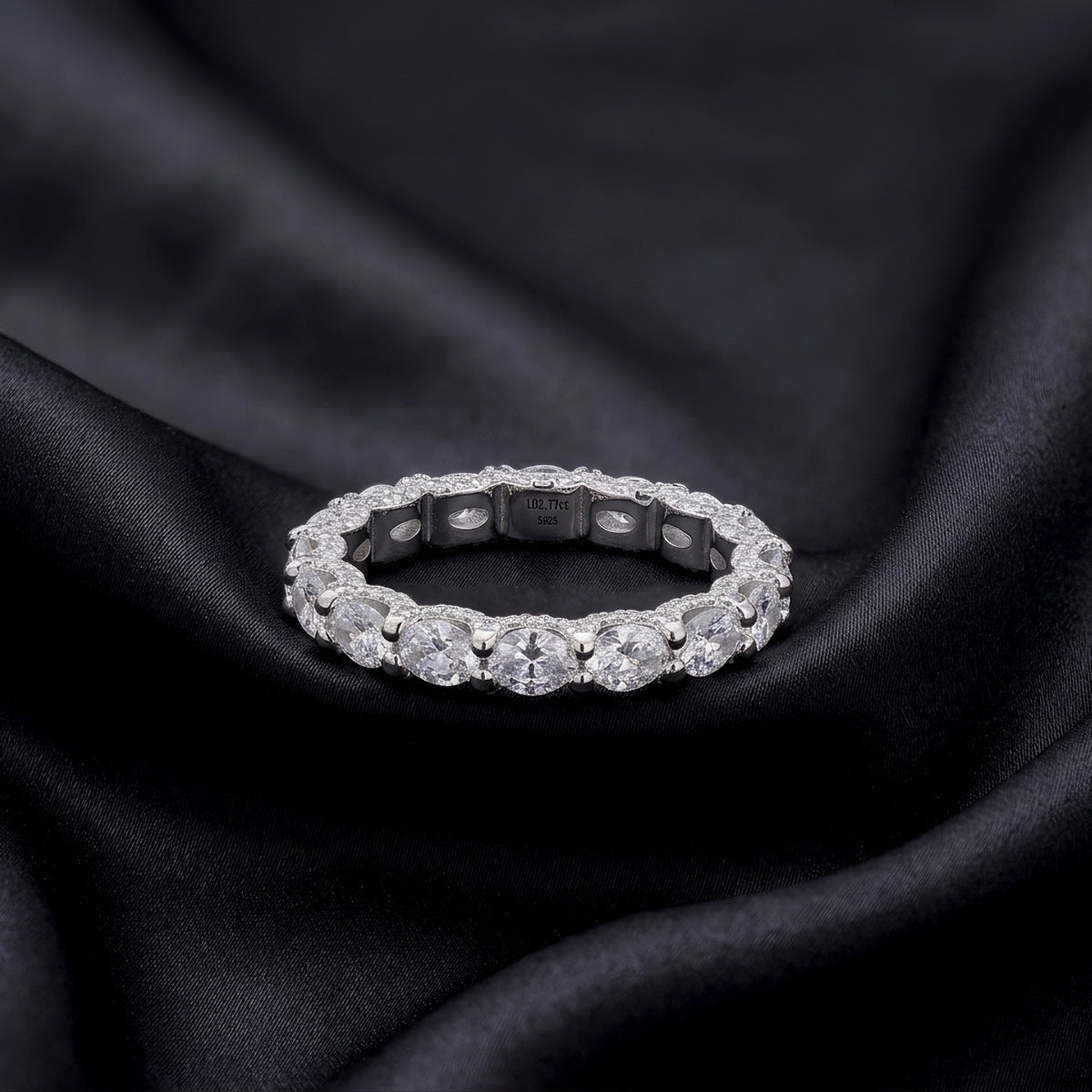 Perspective view of oval cut lab-grown diamond eternity band ring on dark silk.