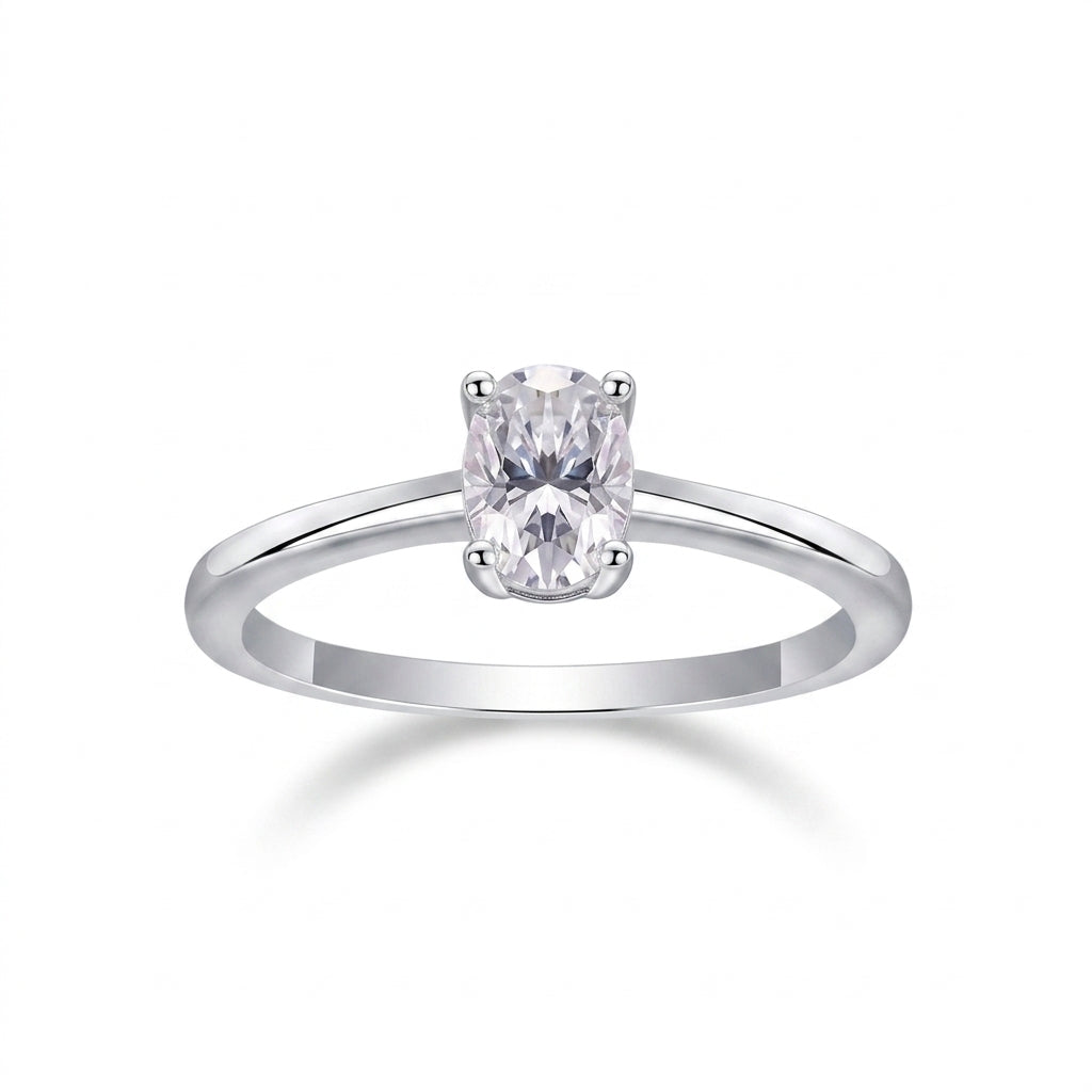 Oval cut moissanite solitaire engagement ring with dainty plain silver band on white background.