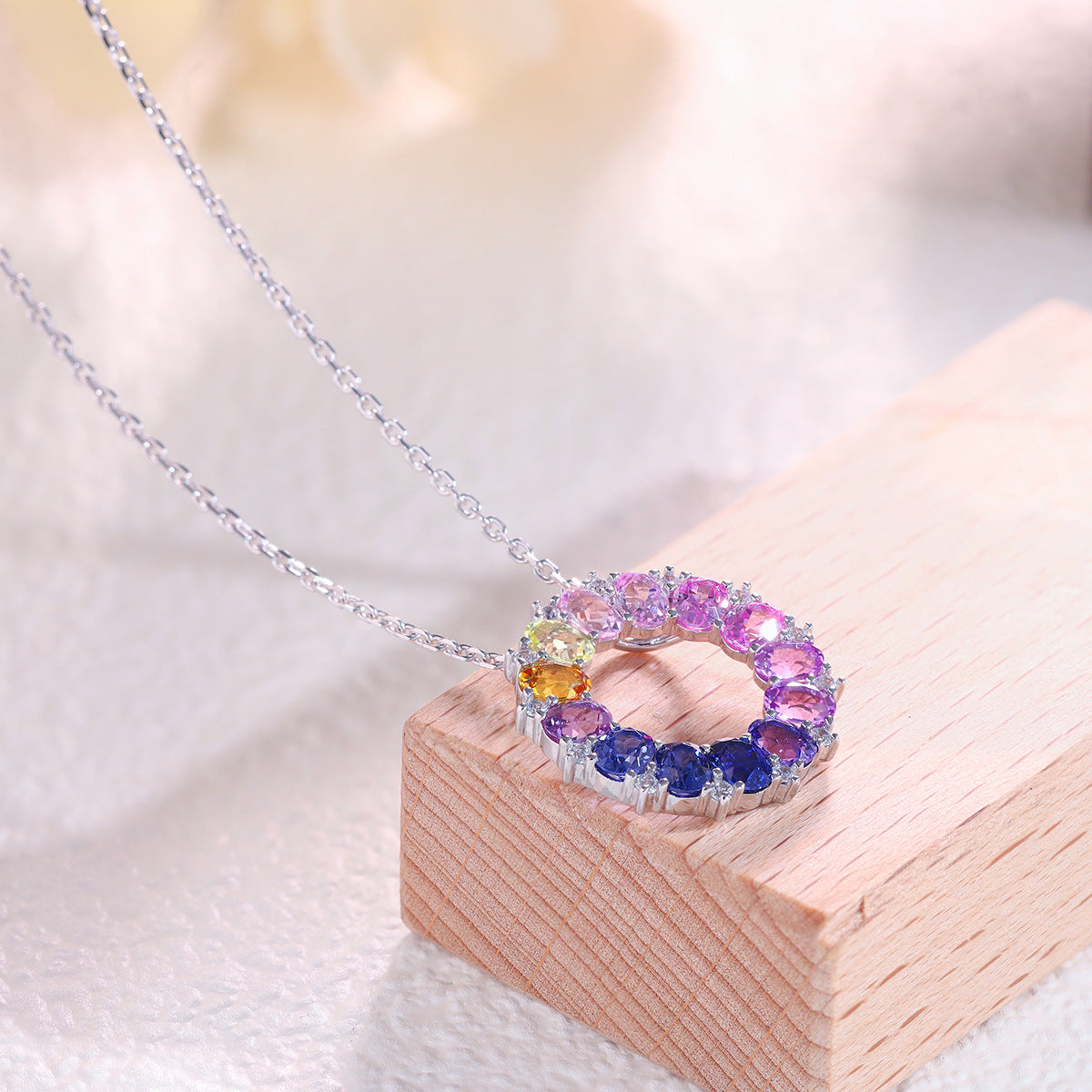 Multi-color oval cut rainbow gemstone circle pendant resting on wooden display block.