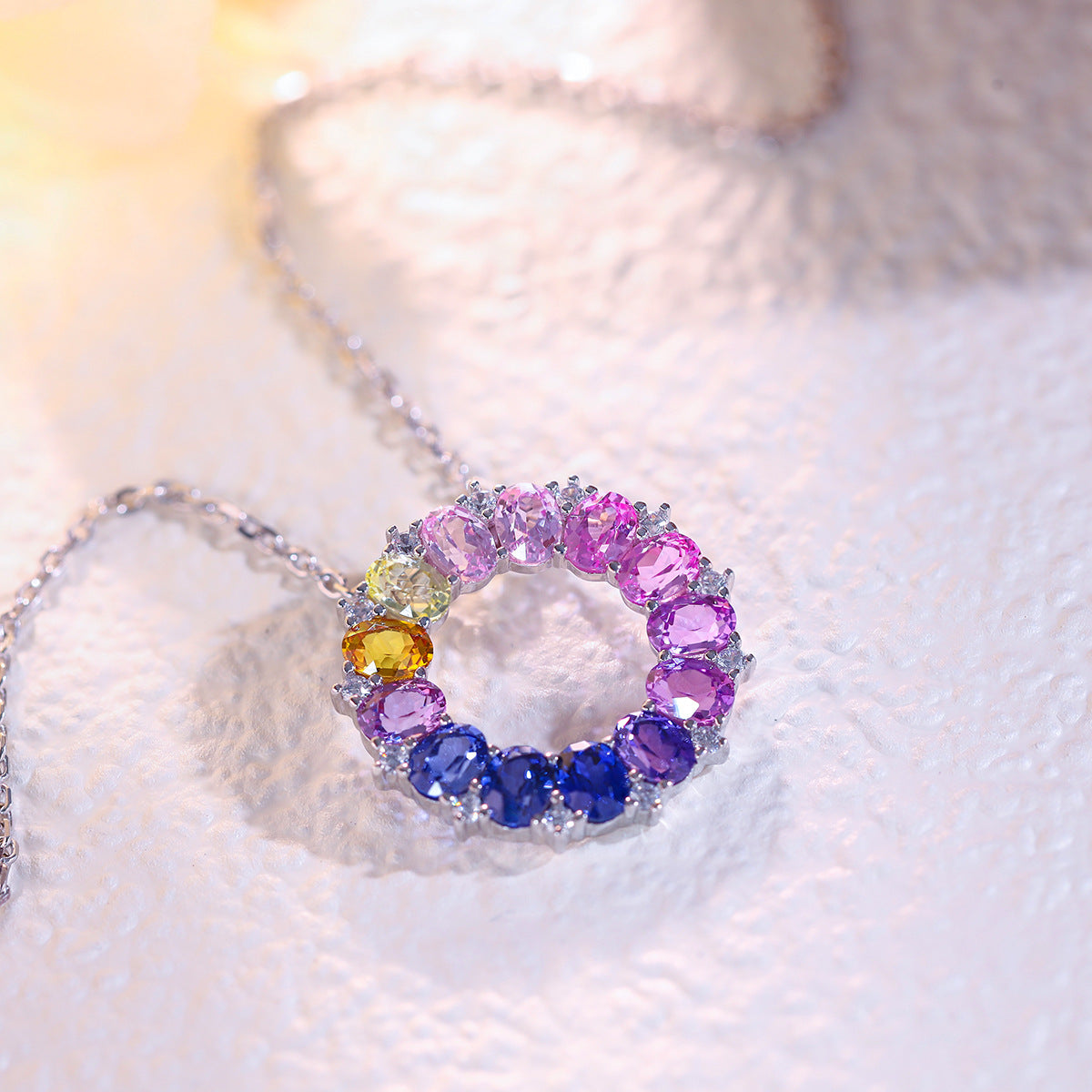 Close-up view of oval cut rainbow gemstone circle pendant showing prong setting and color gradient.