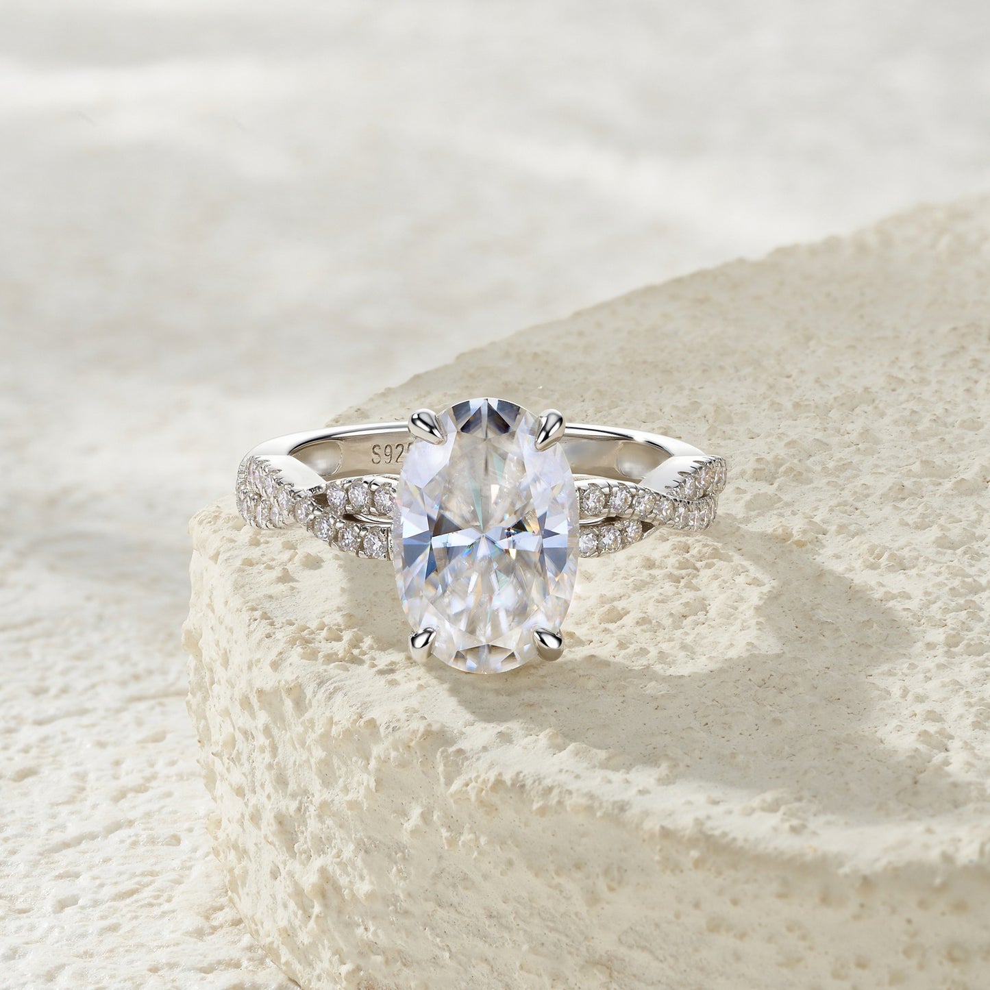 Oval cut moissanite infinity ring resting on textured stone surface.