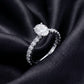 Oval solitaire engagement ring with pave band set against dark silk background.