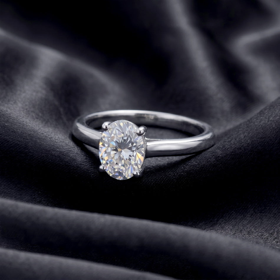 Angled top view of oval cut lab grown diamond plain solitaire ring resting on dark silk.