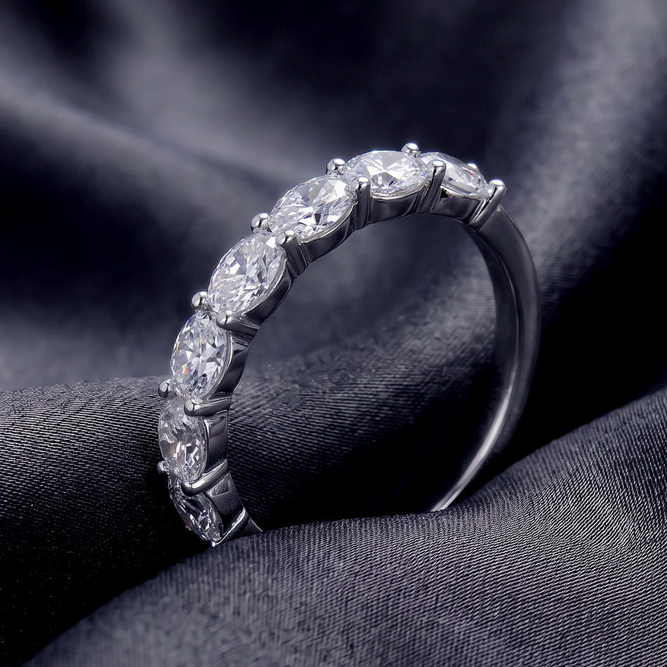 Angled perspective view of oval seven-stone wedding band resting on dark silk.