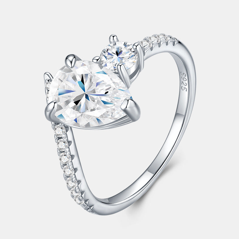 Pear cut and round moissanite toi et moi engagement ring with pave shank on white background.