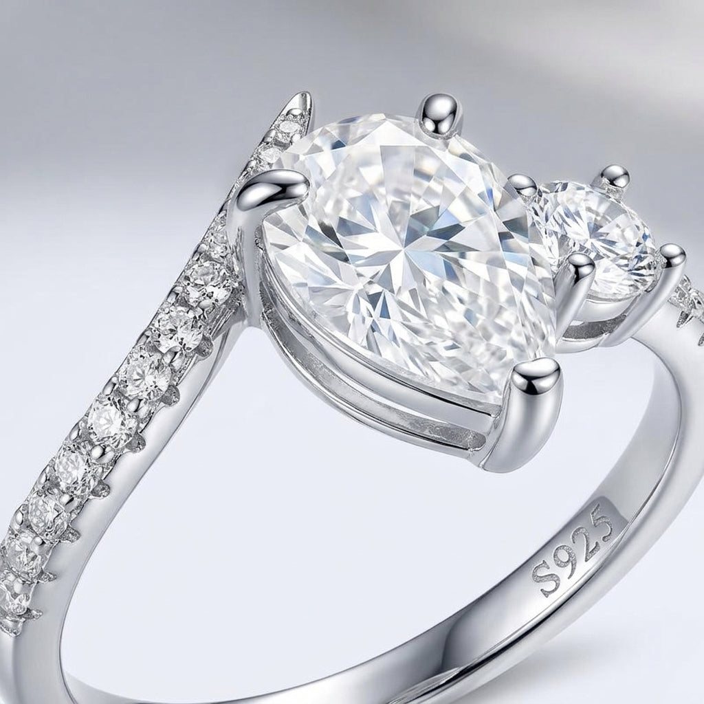 Macro view showing V-prong pear setting and accent round stone on silver moissanite toi et moi ring.