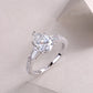 Silver pear cut moissanite ring with baguette accents resting on a smooth background.