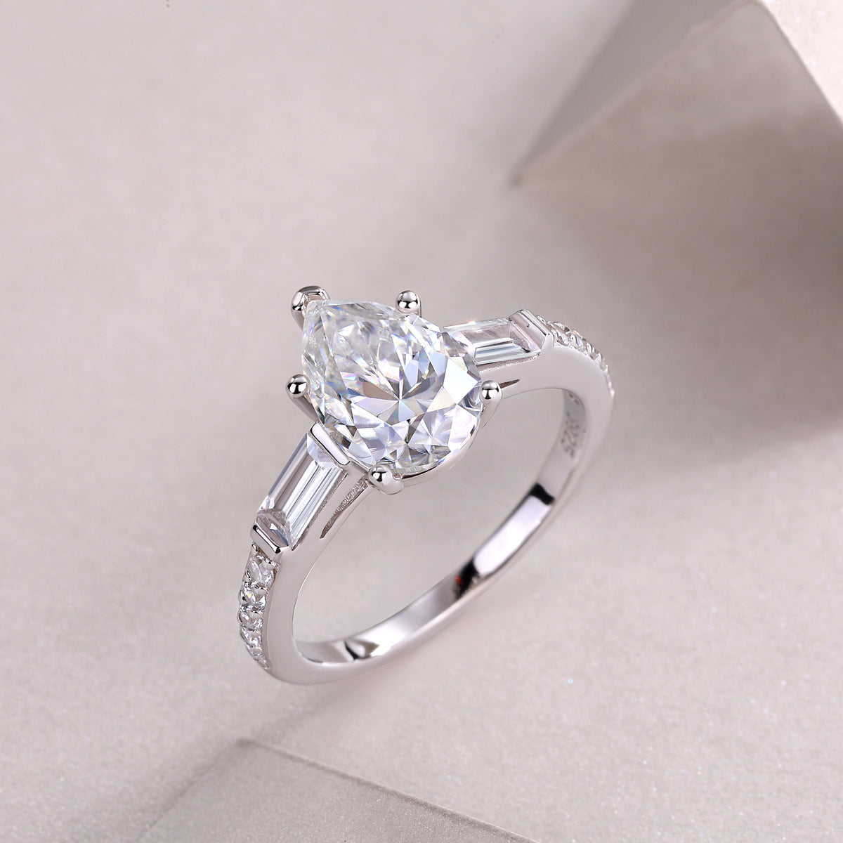 Silver pear cut moissanite ring with baguette accents resting on a smooth background.