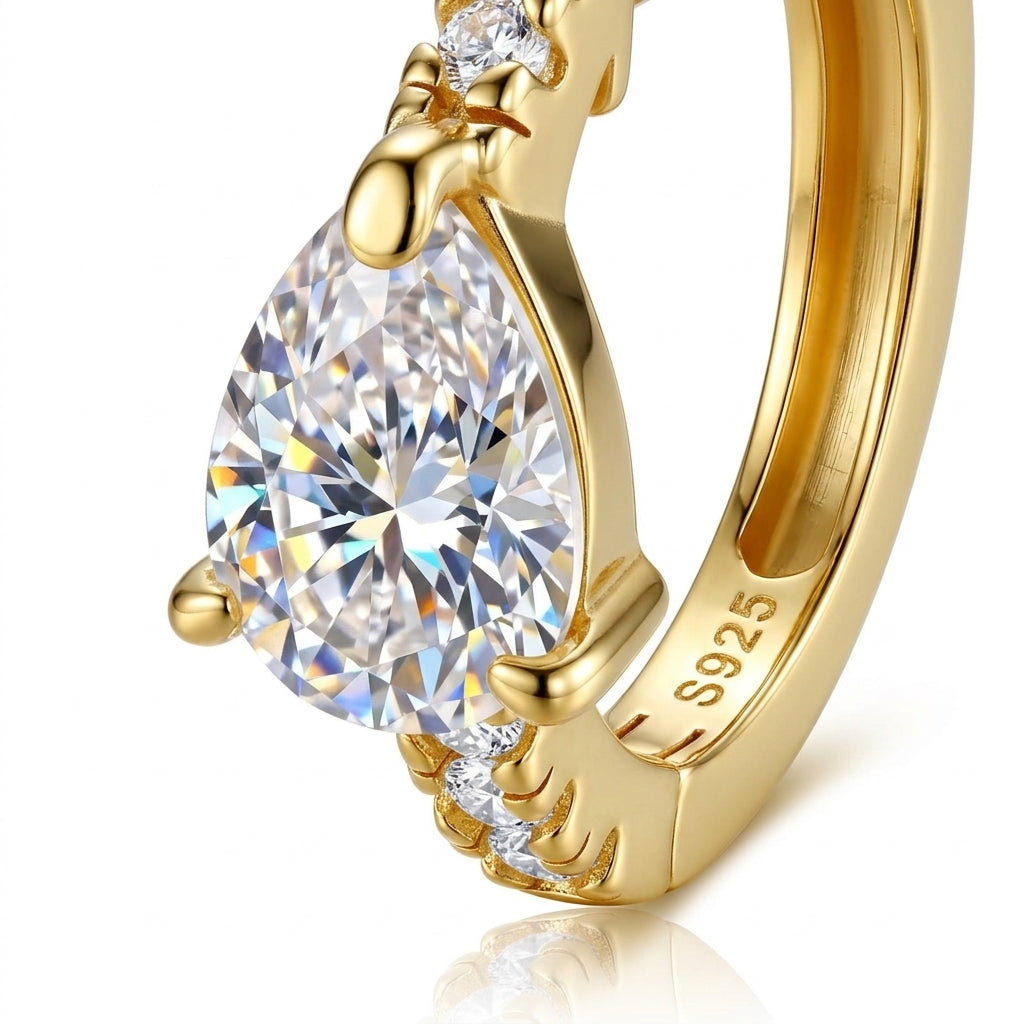 Macro close-up showing prong setting of pear cut moissanite and S925 hallmark on gold huggie hoop.