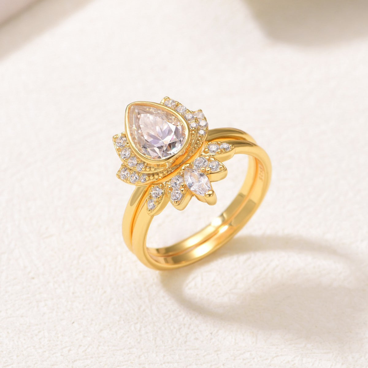 Perspective view of 18K gold plated pear cut moissanite lotus halo and crown ring set.