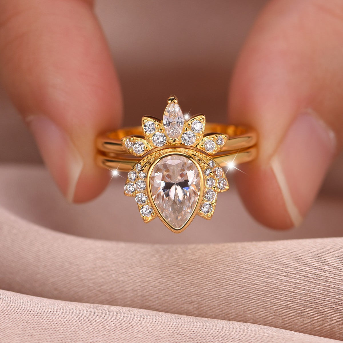 Close-up view of gold pear cut lotus halo solitaire with matching sunburst crown band held in hand.