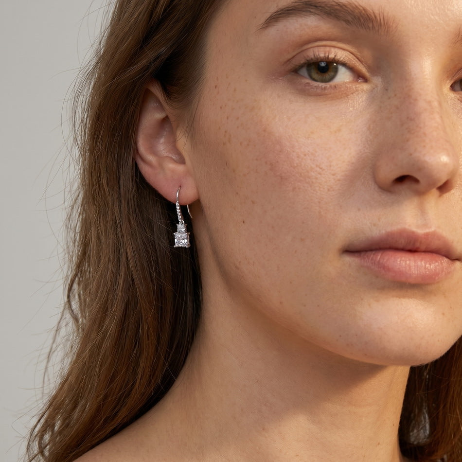 Model wearing princess cut two-stone dangle earrings with pavé line French wire.
