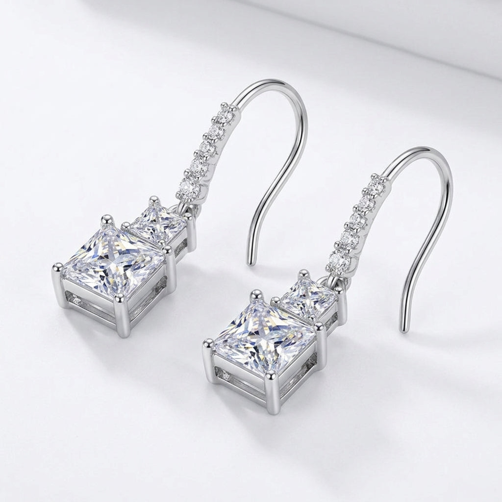 Angled flat lay view of princess cut two-stone dangle drop earrings with pavé hook.