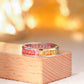 Rainbow baguette gemstone channel set eternity band on wooden stage.