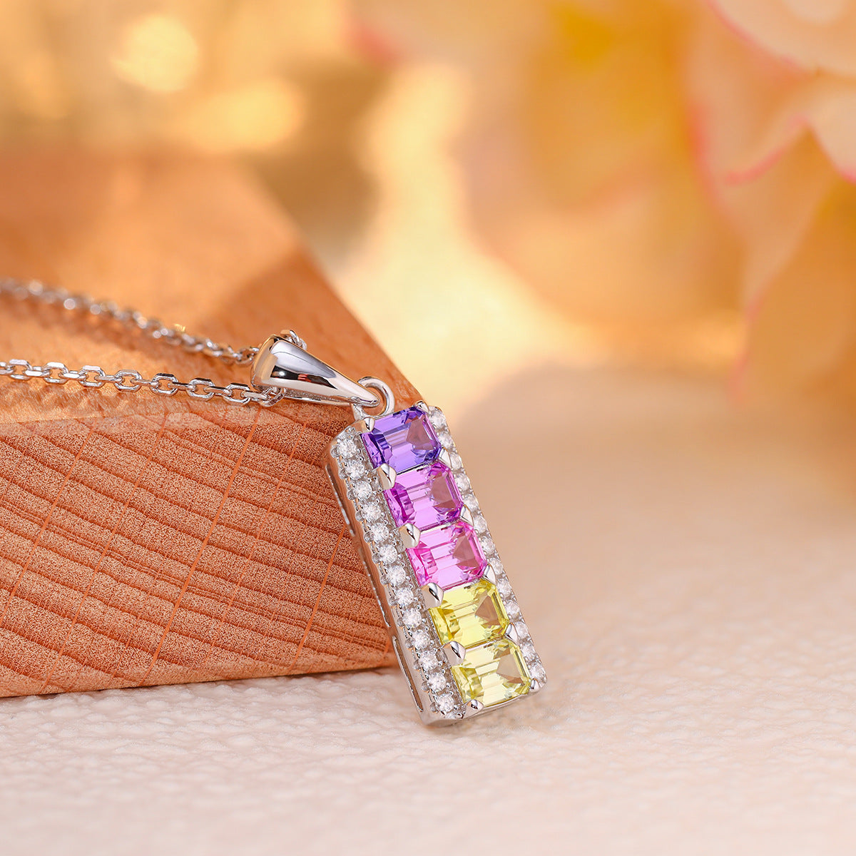 Close-up side view showing pave borders of rainbow emerald cut gemstone vertical bar pendant.