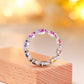 Frontal view of rainbow spectrum oval moissanite eternity ring with twisted pave ribbon.