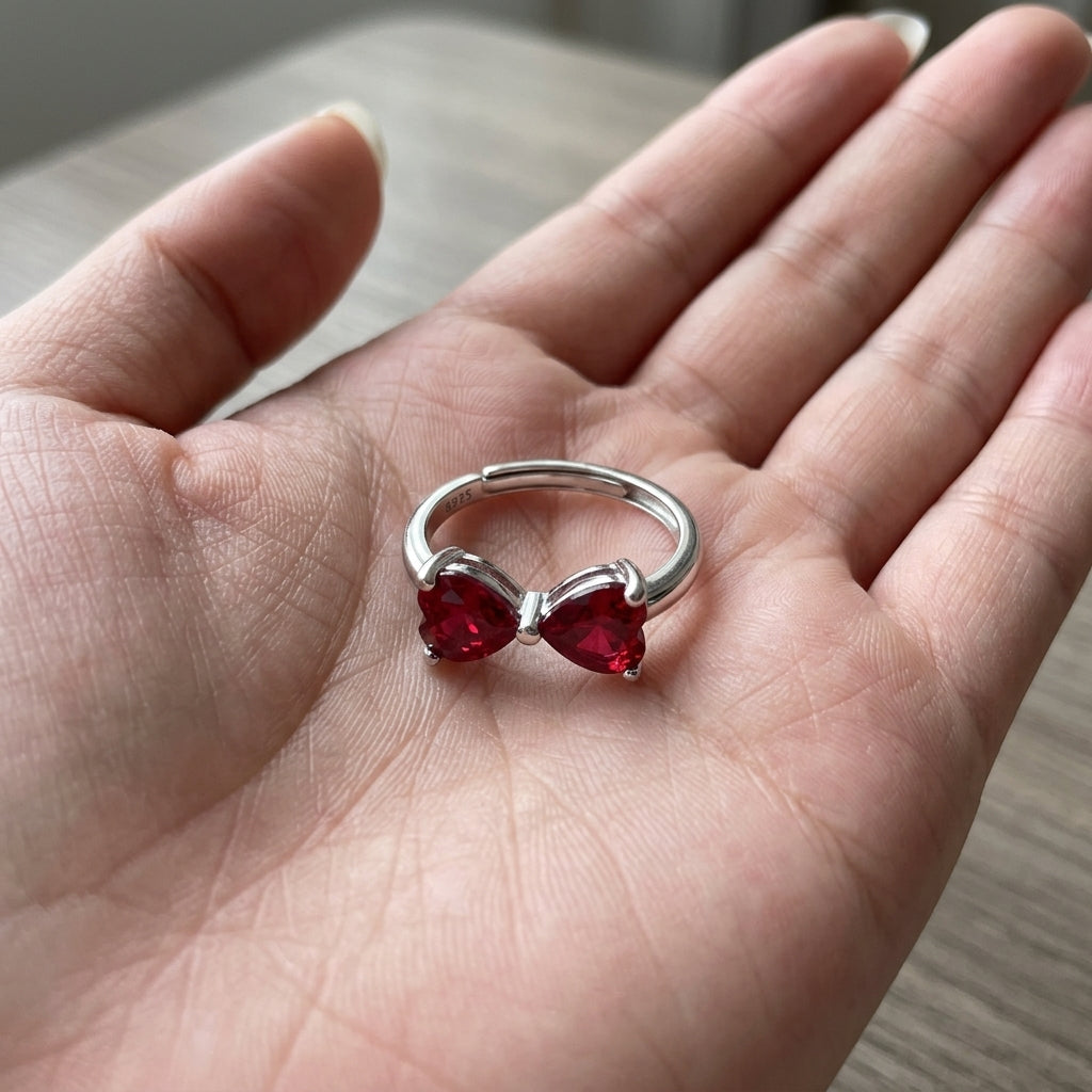 Handheld view in the palm under natural light capturing a romantic heart-cut ruby bow-knot adjustable ring.