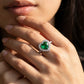 Close-up of a model showcasing a romantic heart-shaped emerald statement ring with a diamond halo on her finger.