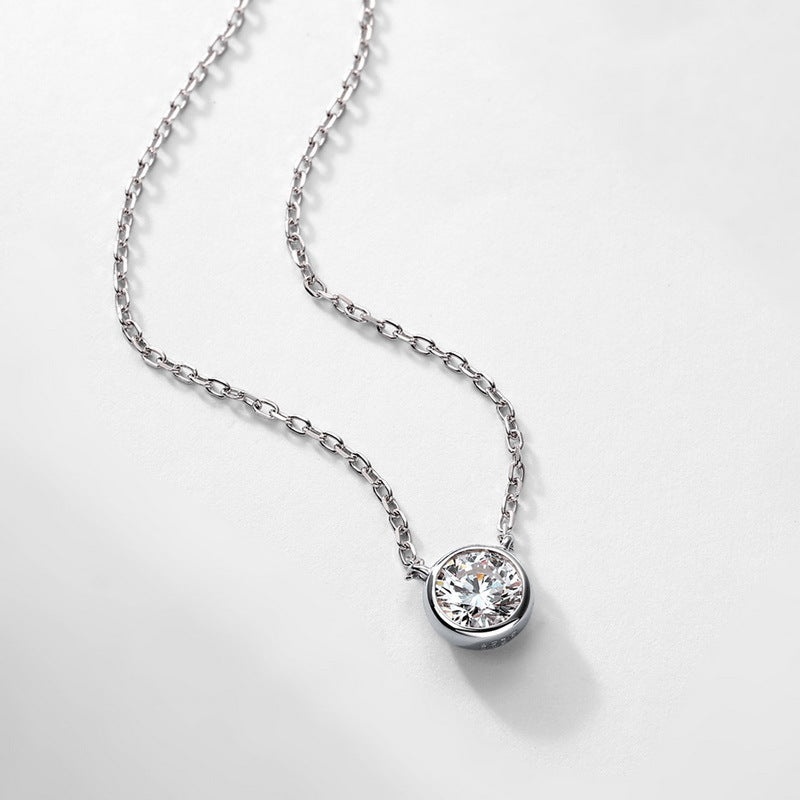 Round bezel set lab grown diamond solitaire necklace lying on light background.