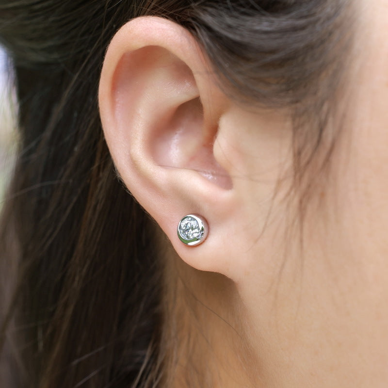 Model wearing round solitaire bezel set diamond stud earring on earlobe.