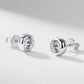 Pair of round bezel set solitaire diamond stud earrings resting on light gray background.