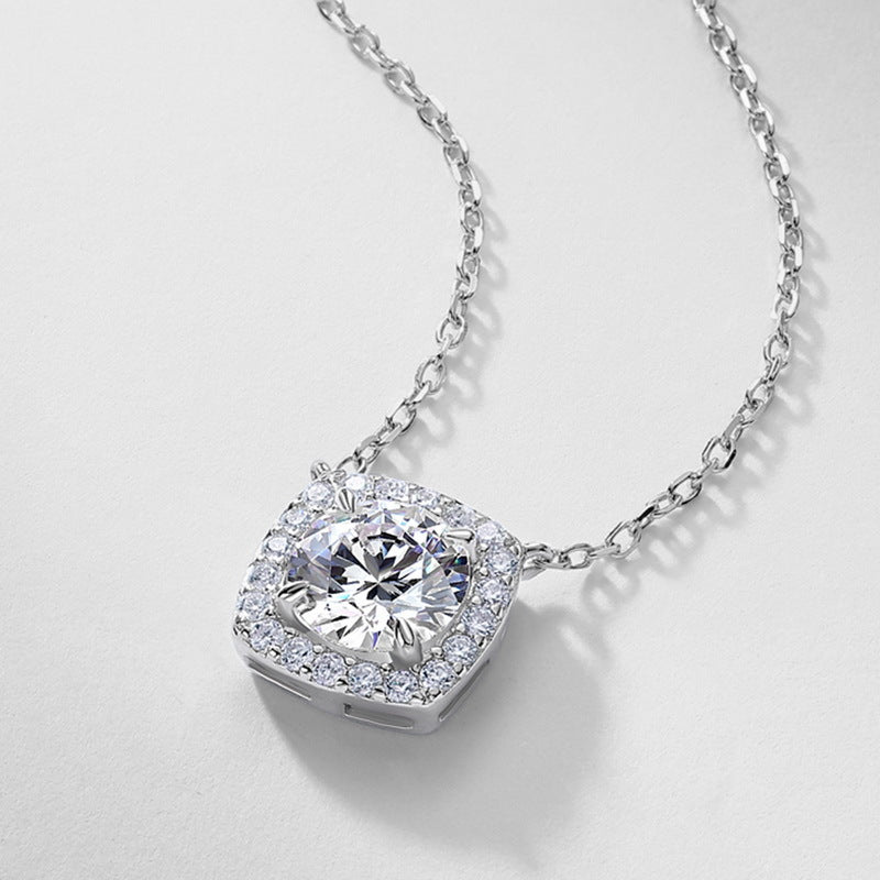 Perspective view of round lab grown diamond cushion halo pendant resting on light gray surface.