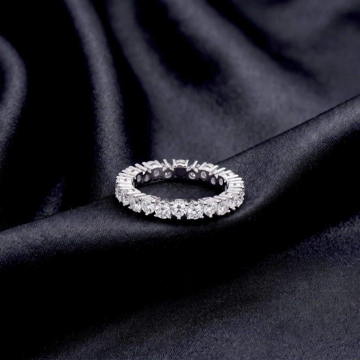 Round brilliant lab grown diamond eternity wedding band resting flat on dark black silk
