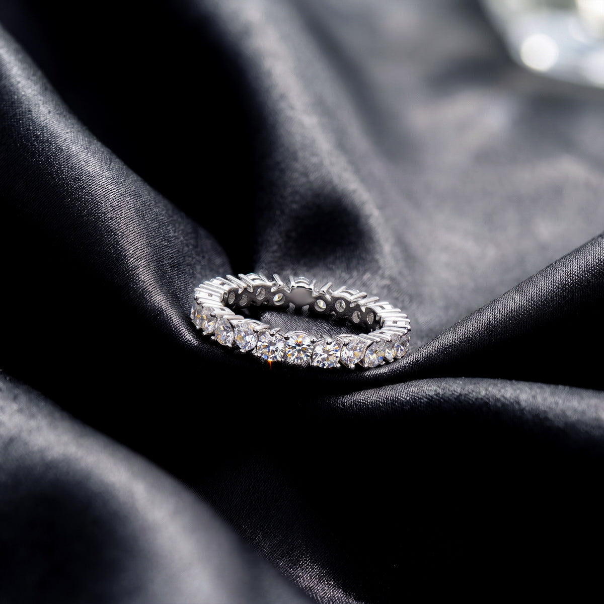 Side profile view showing shared prong setting of round lab grown diamond eternity ring on black silk