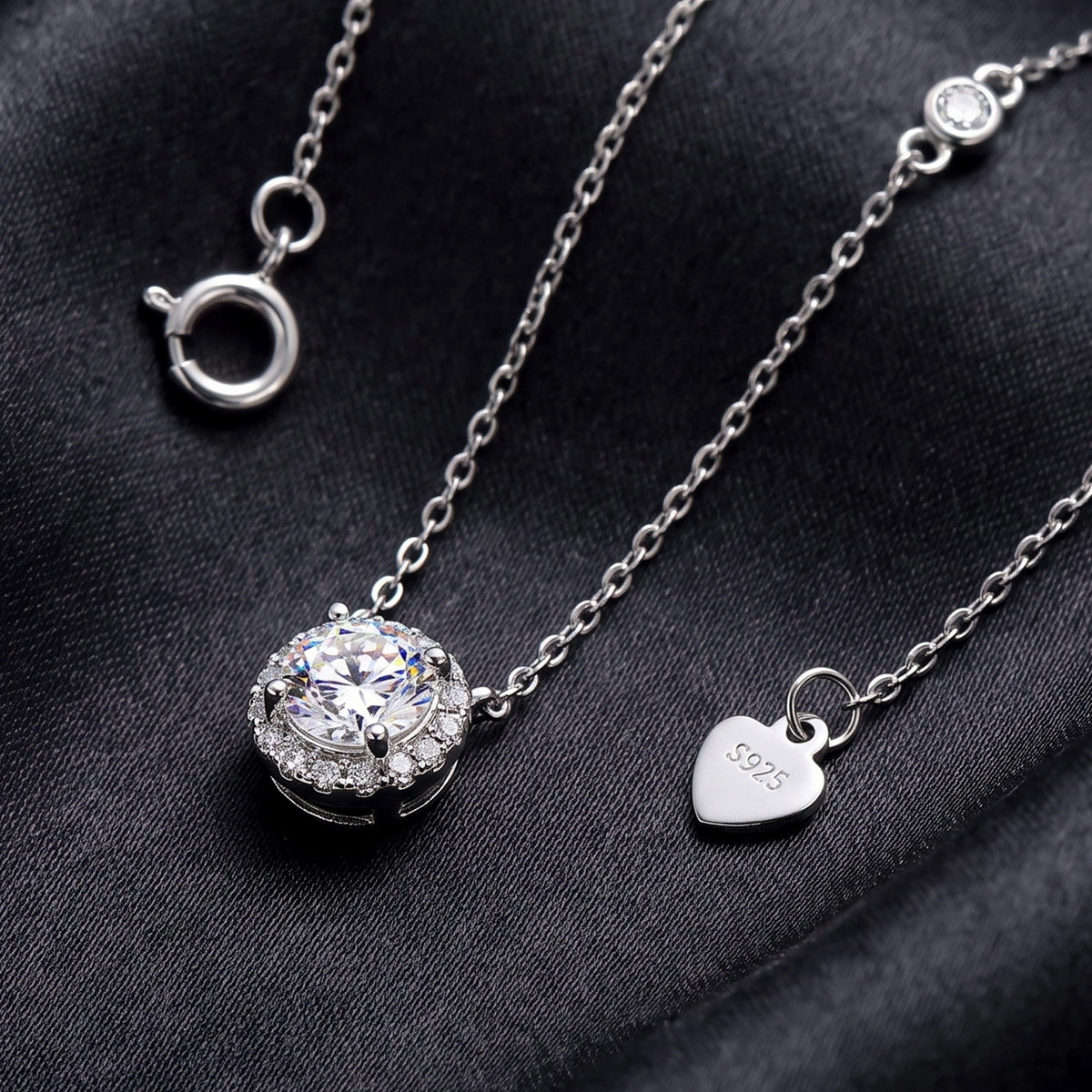 Close up view of round cut lab grown diamond halo pendant and S925 heart tag on dark black silk