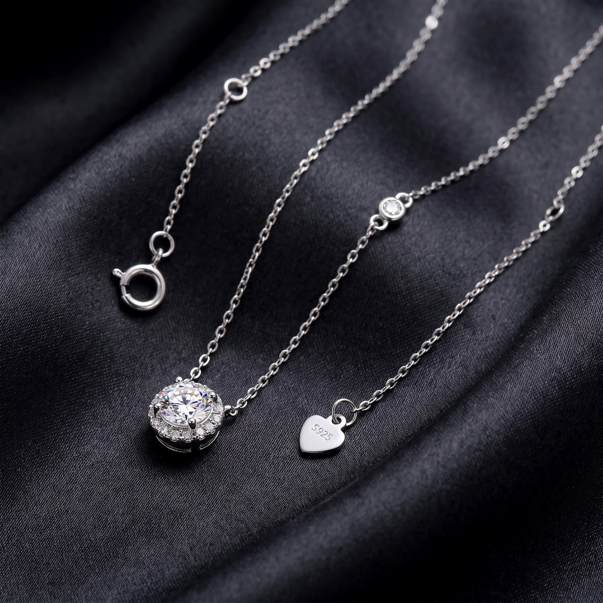 Round cut lab grown diamond halo pendant necklace showing chain and clasp on dark black silk