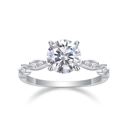 Round cut moissanite engagement ring with marquise leaf station shank on white background.