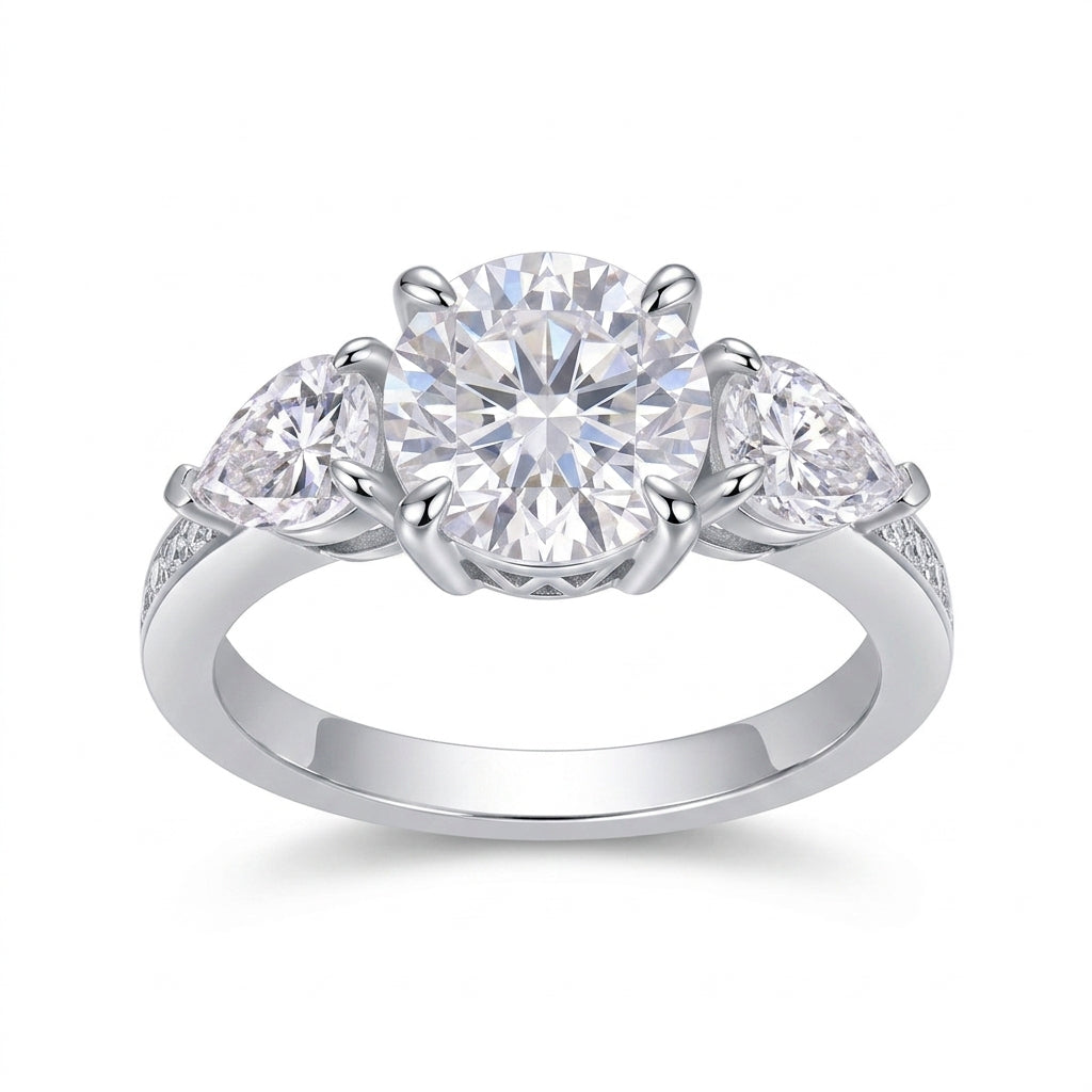 Round cut moissanite three stone engagement ring with pear-shaped side stones on white background.