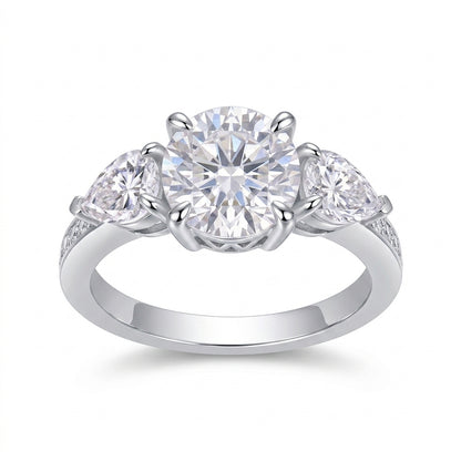 Round cut moissanite three stone engagement ring with pear-shaped side stones on white background.