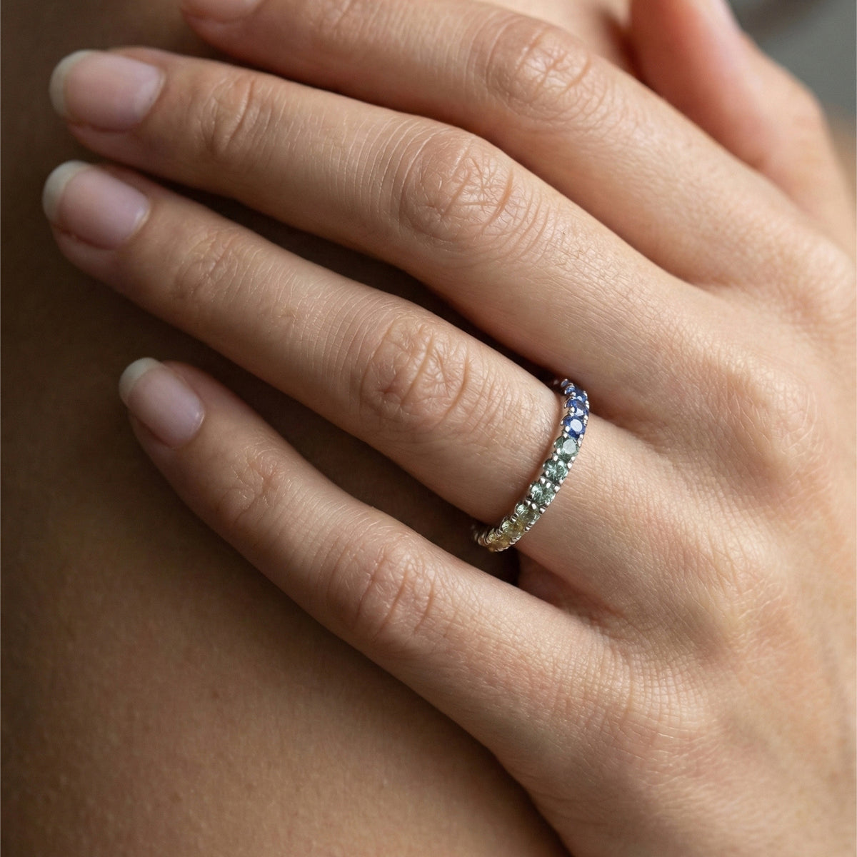 Model wearing gold round cut rainbow gradient pave gemstone eternity band ring on hand