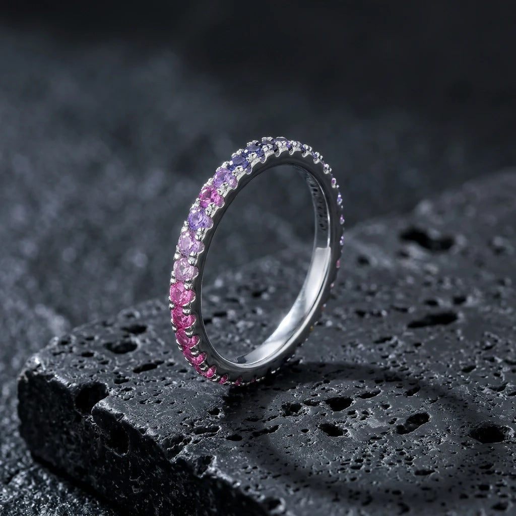 Silver round cut rainbow gradient pave eternity band ring on textured black volcanic stone surface