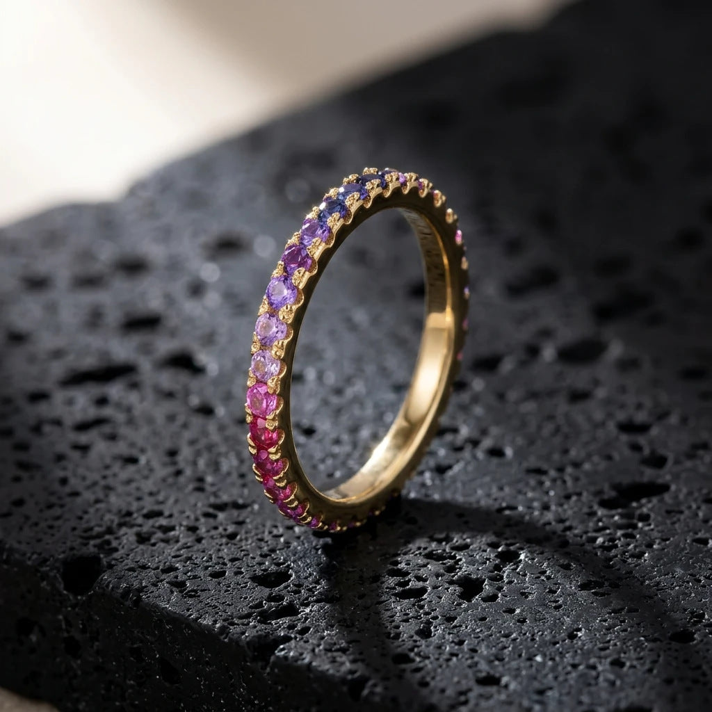 Gold round cut rainbow gradient pave eternity band ring on textured dark stone surface with dramatic lighting