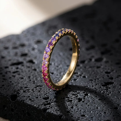 Gold round cut rainbow gradient pave eternity band ring on textured dark stone surface with dramatic lighting