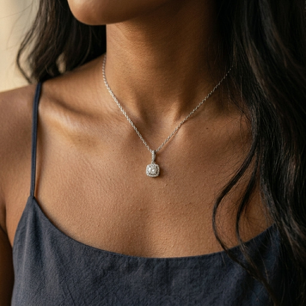 Model hand near chest wearing round diamond cushion halo pendant necklace with dark slip dress.