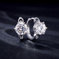 Pair of six-prong round diamond solitaire huggie hoop earrings on black backdrop.