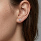 Model wearing round cut diamond solitaire stud earrings with heart prongs on earlobe.