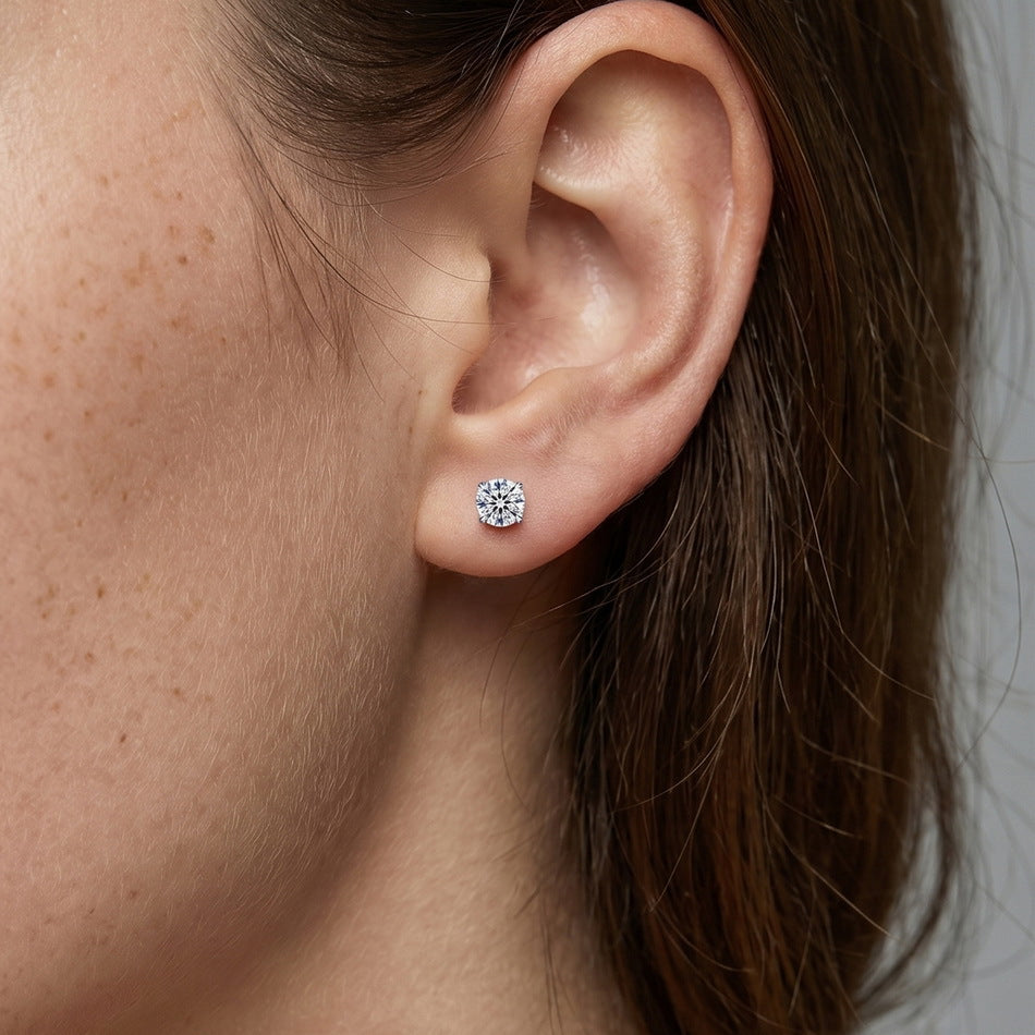 Model wearing round cut diamond solitaire stud earrings with heart prongs on earlobe.