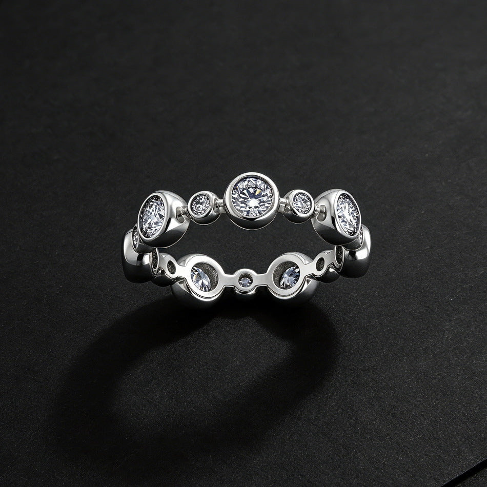 Round cut lab diamond bezel set alternating bubble eternity ring on dark textured background.