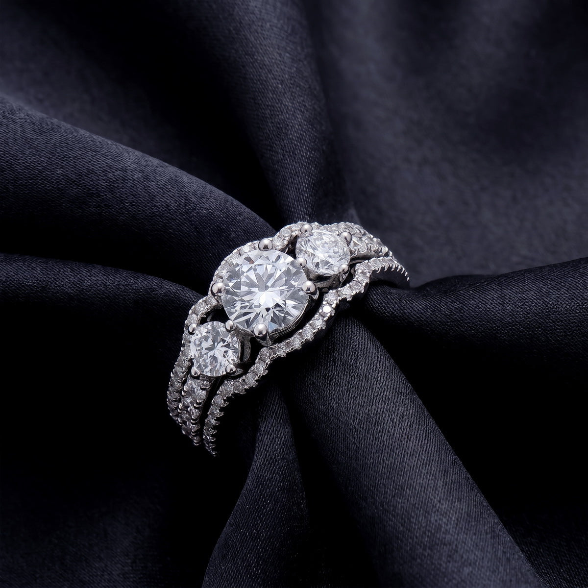 Perspective view of round lab-grown diamond 3-stone bridal ring set on dark silk.