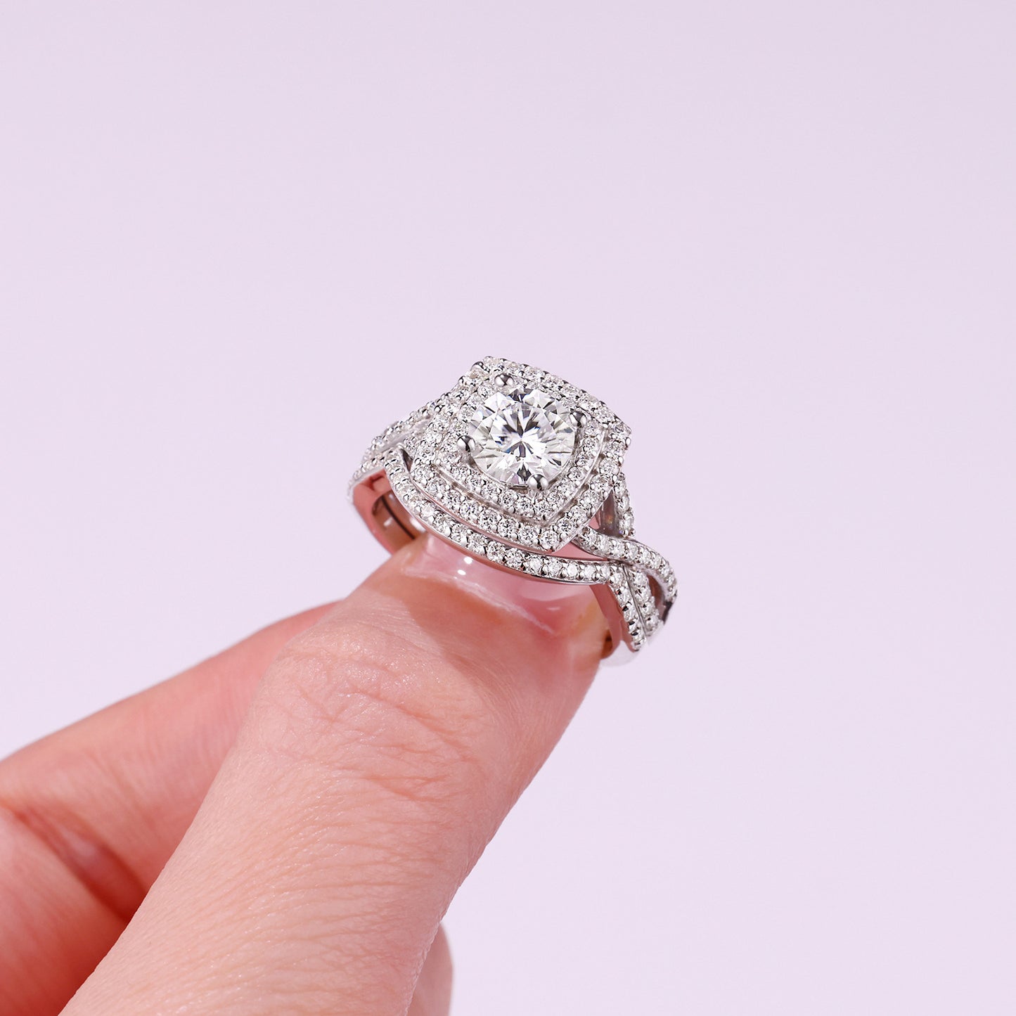 Handheld close-up showing double cushion halo and twisted split shank on silver moissanite ring.