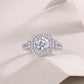 Round moissanite cushion double halo ring resting on textured light surface.