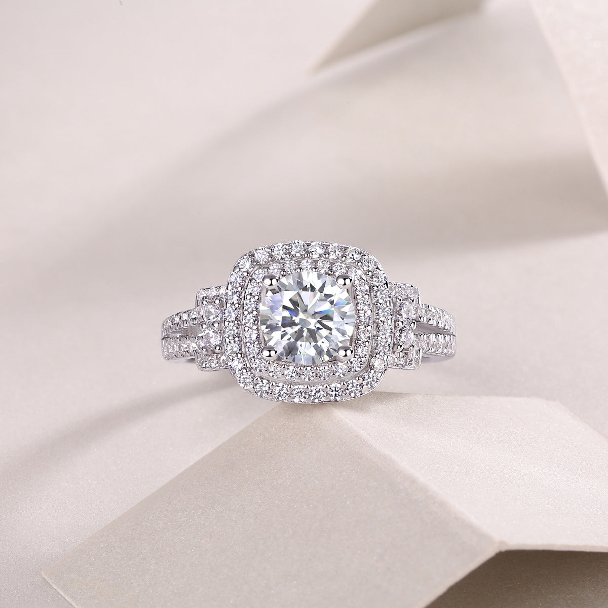 Round moissanite cushion double halo ring resting on textured light surface.