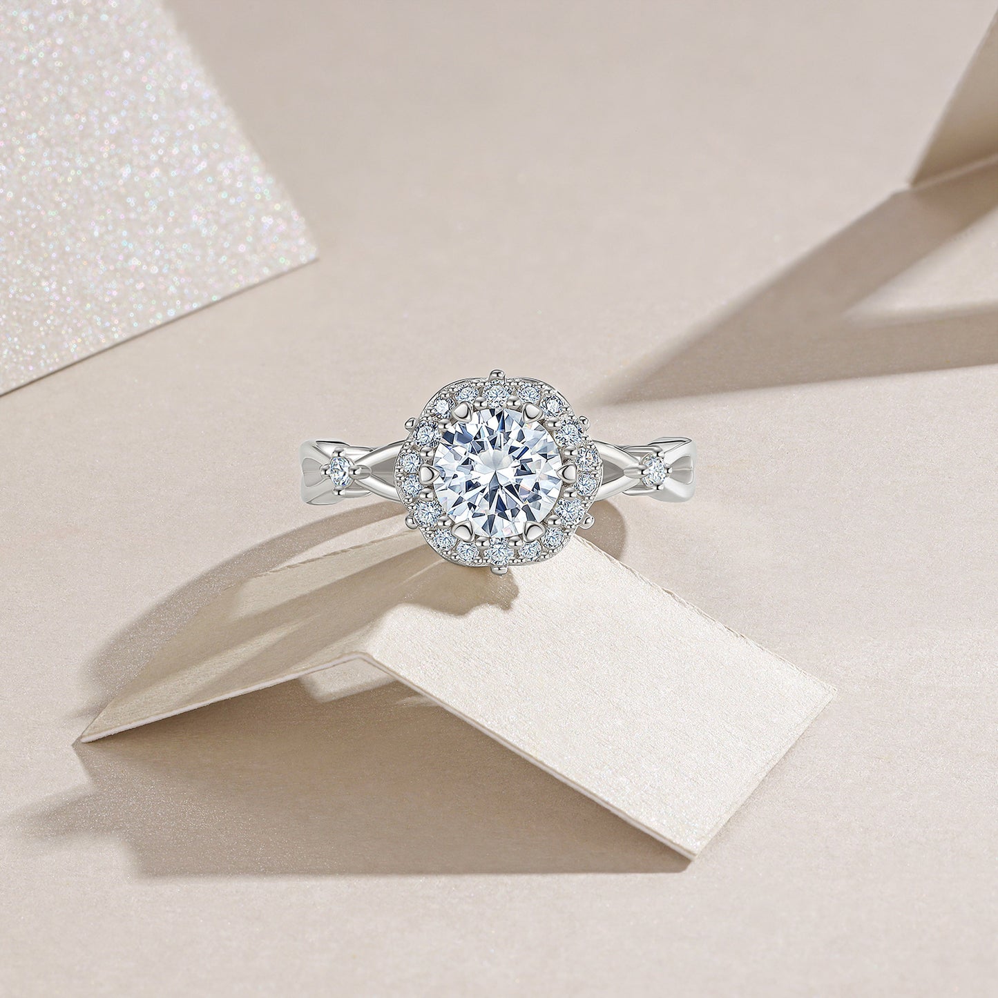 Round moissanite floral halo engagement ring resting on textured white background.
