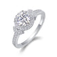 Silver round moissanite engagement ring with geometric halo accent band standing on white surface.