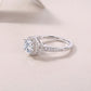 Silver round moissanite ring with geometric shoulder accents on a light blue background.